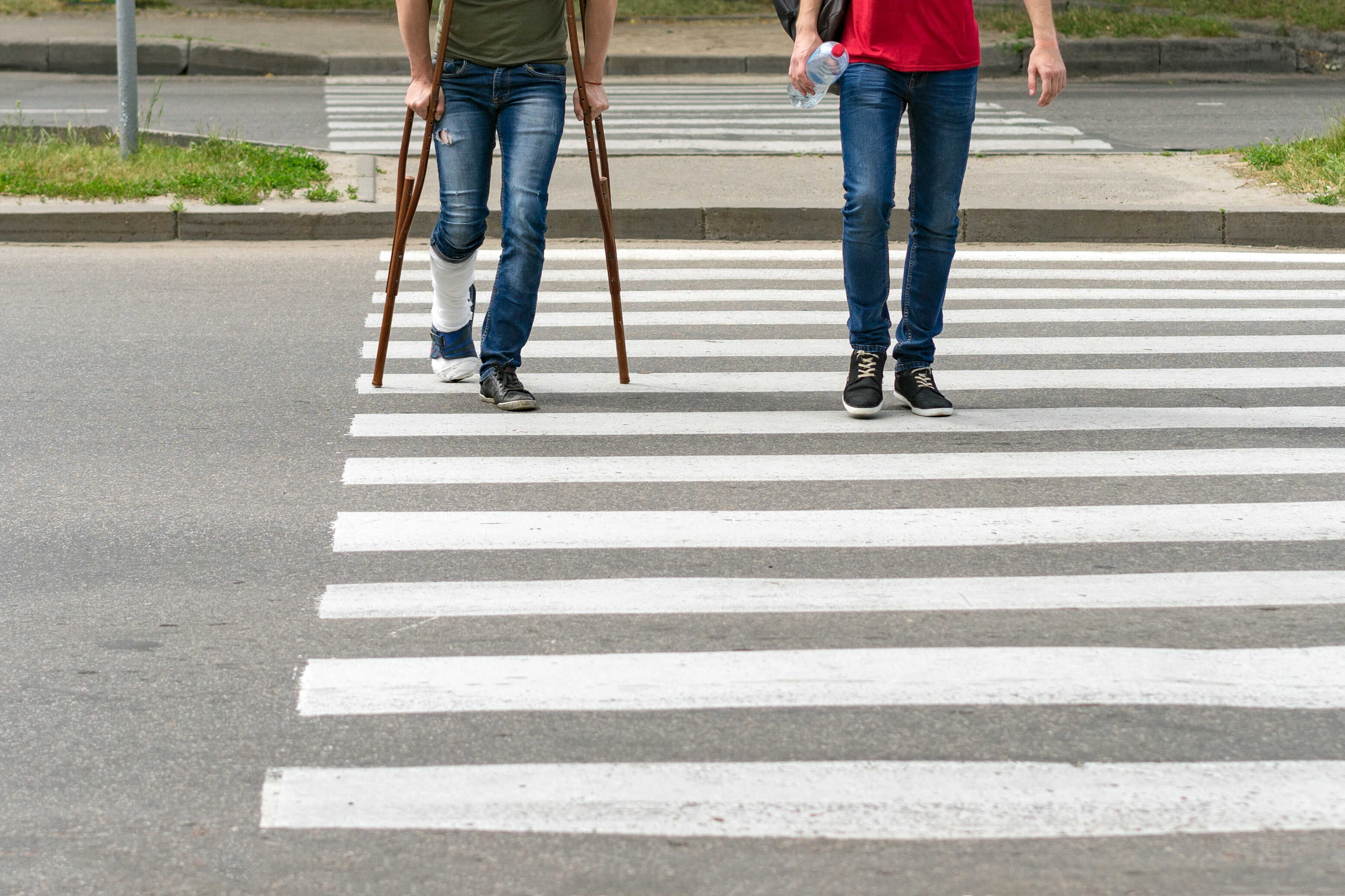 an injured person walking across crosswalk on crutches with friend